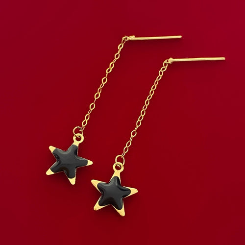 Gold chain earrings with black star charms on red background, elegant jewelry design